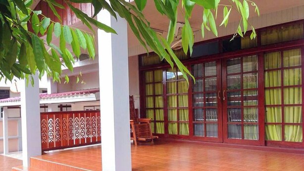 A spacious indoor area with a tiled floor, a staircase leading to an upper level, and a large window with green curtains. - Buriram The Big House Intown (Buriram)