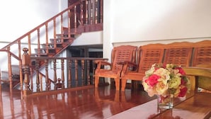 A wooden staircase with a polished floor, wooden chairs, and a vase with flowers on a table. - Buriram The Big House Intown (Buriram)
