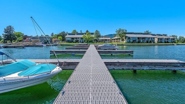 A marina with docked boats, a wooden pier leading to a building complex with multiple stories and balconies.