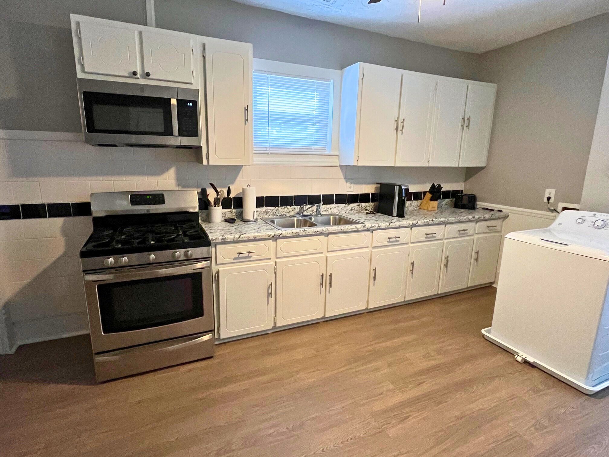 A kitchen with white cabinets, a stove, a microwave, a sink, and a washing machine.