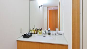 Casa de banho com um espelho grande, lavatório branco, armários de madeira e produtos de higiene pessoal.