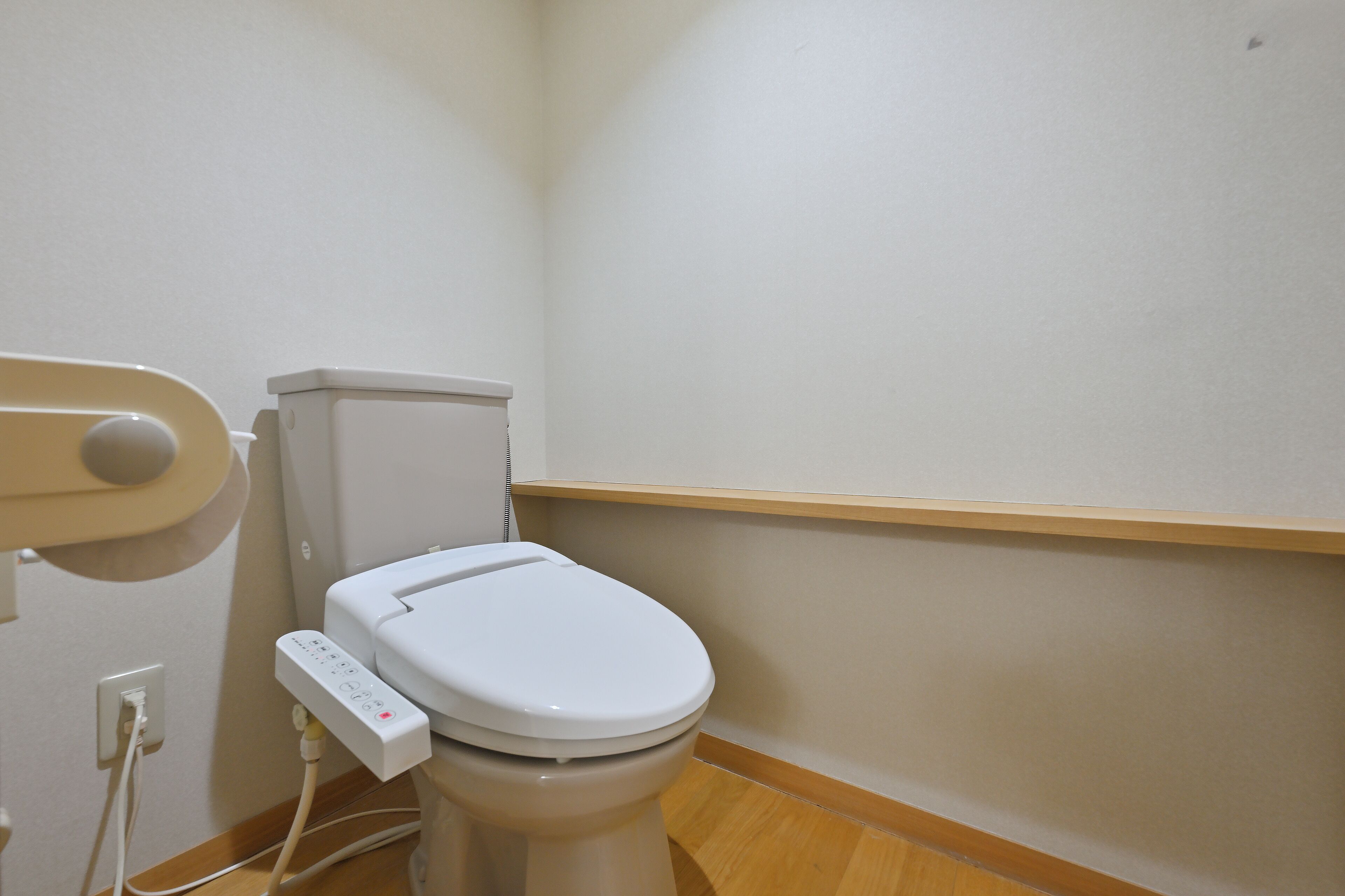 WC, jossa on ohjauspaneeli, seinälle kiinnitetty hylly ja puulattia.