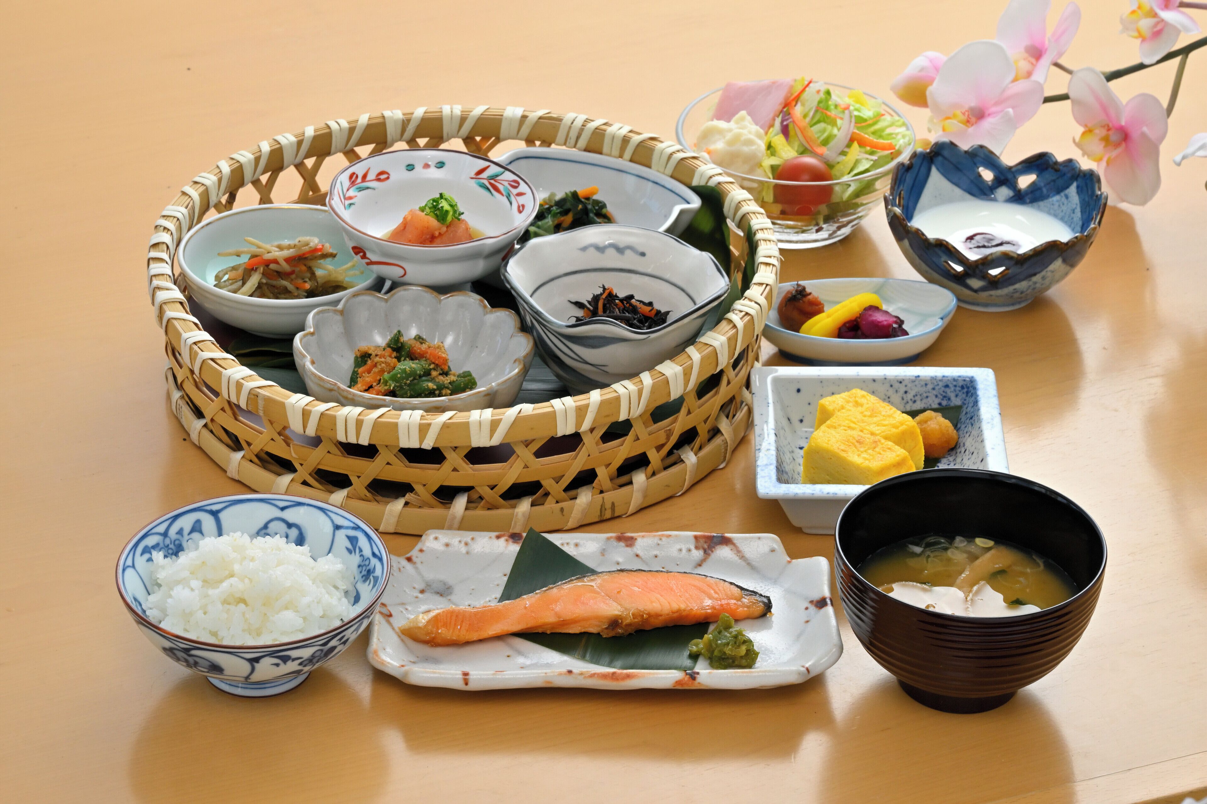 A variety of dishes including rice, salmon, and soup, arranged on a table with a woven basket and several bowls.