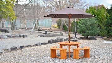 A wooden table and bench set with an umbrella in a gravel area surrounded by rocks and trees.