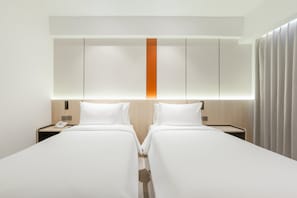 Een hotelkamer met twee eenpersoonsbedden, een houten hoofdbord met een verticale oranje accentkleur, en een nachtkastje met een telefoon.