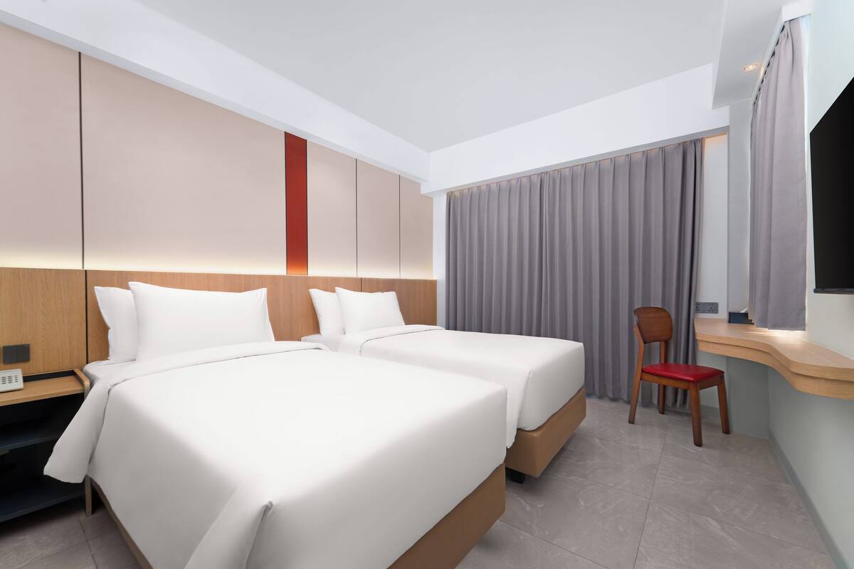 A hotel room with two beds, a desk, a chair, and a TV.