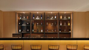 A bar area with multiple shelves of liquor bottles and glasses, and four bar stools. - MAXONE Batam (Batam)