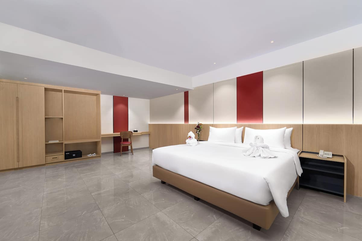 A modern hotel room with a large bed, built-in wardrobe, and a desk area.