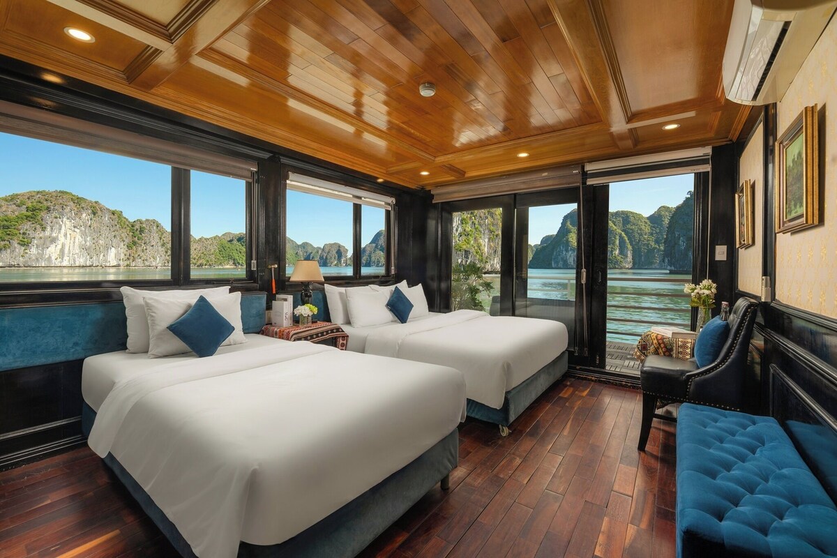 A room with two beds, a blue bench, and large windows offering a view of a mountainous landscape.