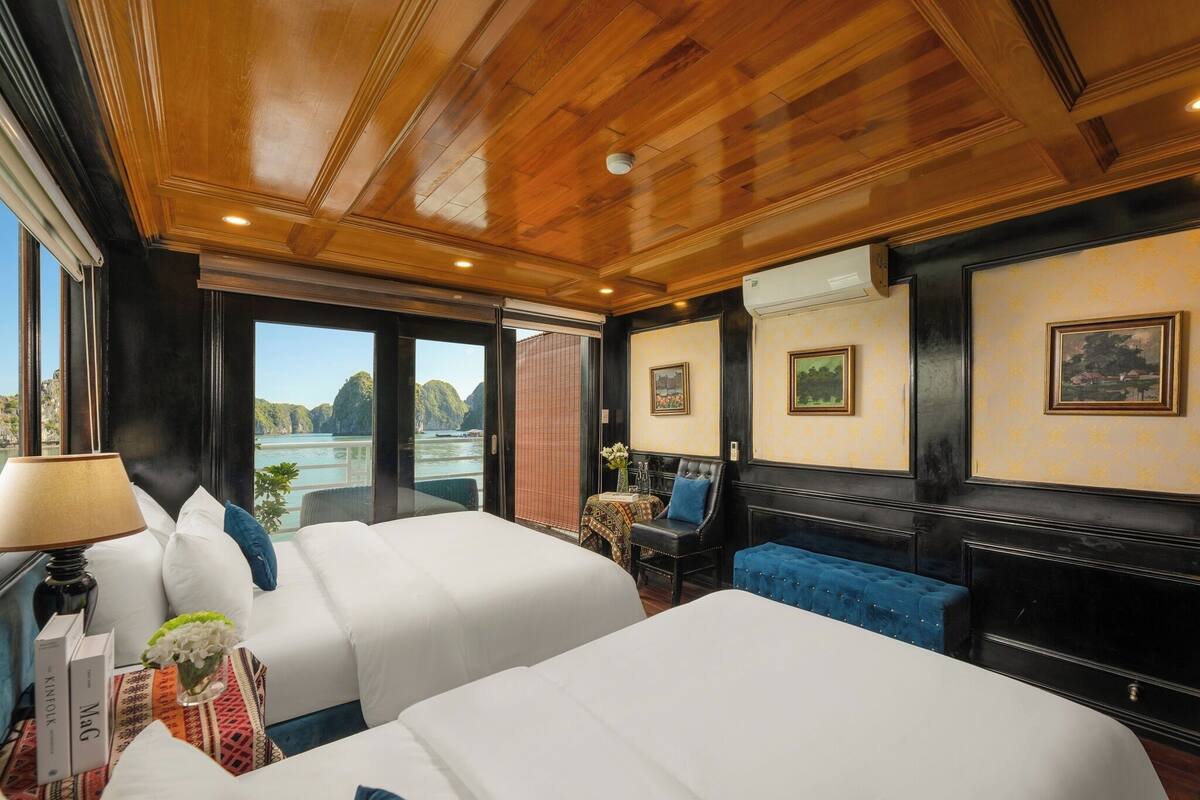 A hotel room with two beds, a blue sofa, a table with a vase of flowers, and a view of the sea.