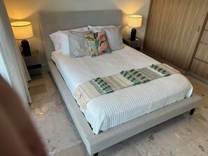 Ein ordentlich gemachtes Bett mit gestreifter Tagesdecke und einer dekorativen Zierdecke, flankiert von zwei Nachttischlampen und einem Nachttisch.