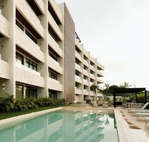 A modern hotel with a pool, multiple balconies, and outdoor seating areas. - Brand New Condo In Beautiful Cozumel - 2 Bedroom/2 Bath With AC and Fitness Room (San Miguel de Cozumel)