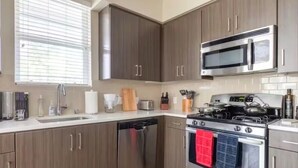 A modern kitchen with stainless steel appliances, wooden cabinets, and a window with blinds. - Luxe Marina Escape-Near SoFi & Beaches (Marina del Rey)