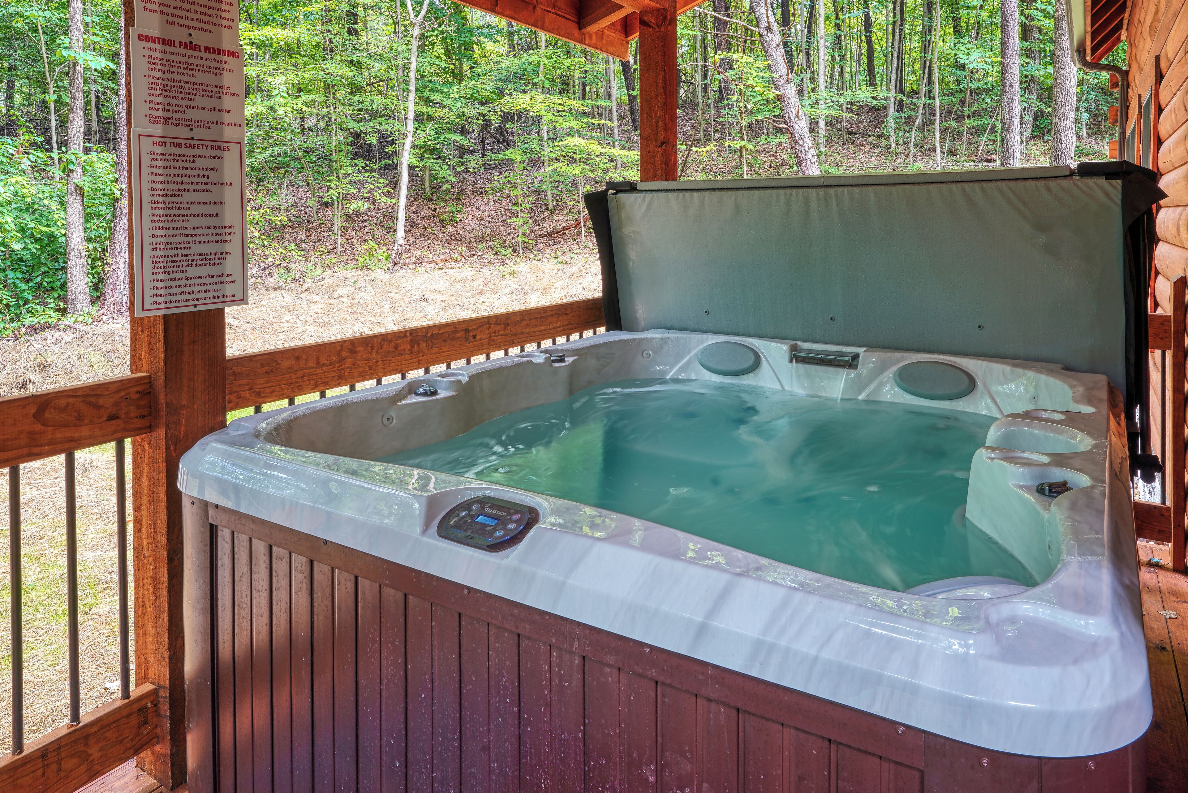 A hot tub with a control panel, surrounded by a wooden deck and a forested area.
