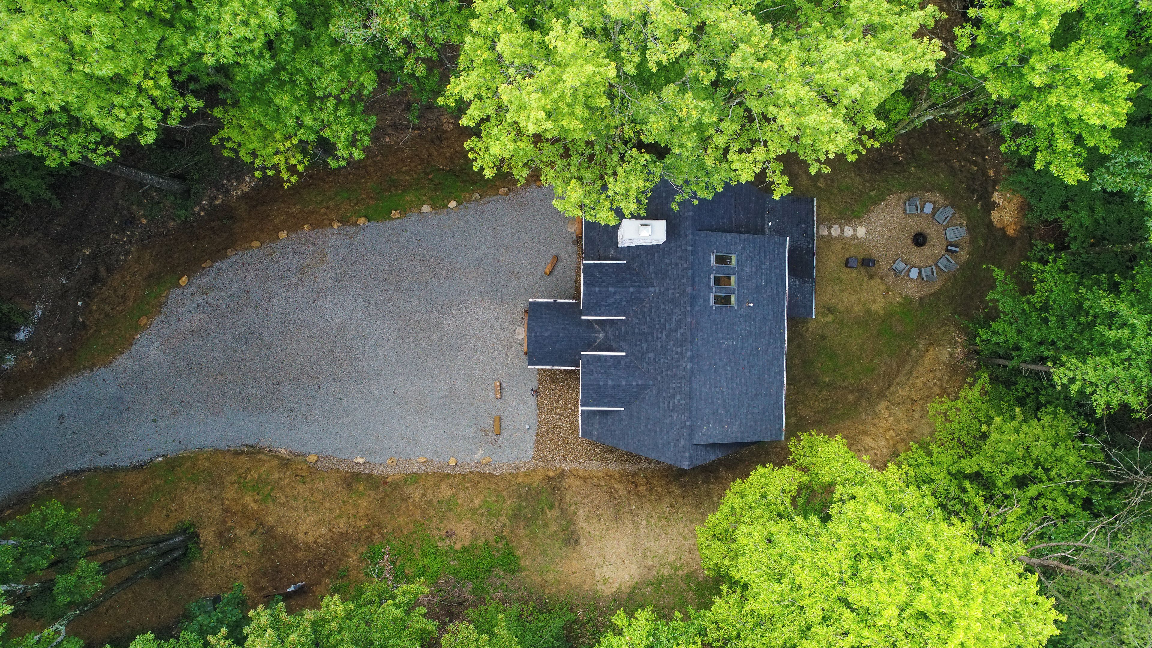 A house with a paved driveway, a circular outdoor seating area, and a large tree in the foreground.