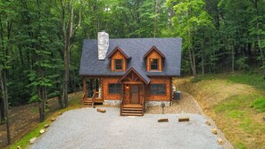 Une cabane en rondins avec une cheminée en pierre, une véranda et une allée gravillonnée.