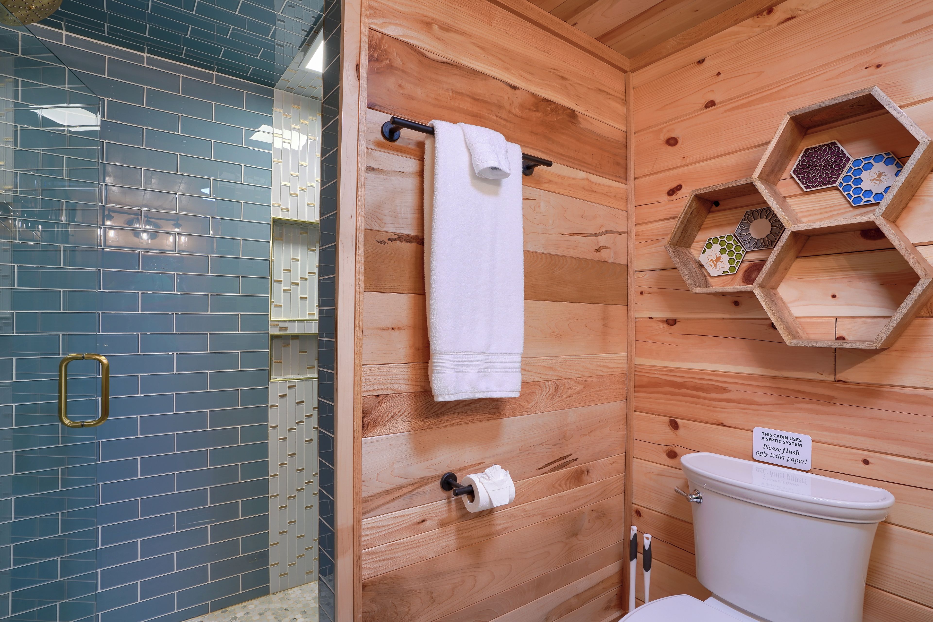 A bathroom with a wooden wall, a glass shower enclosure, a toilet, and a shelf with decorative items.