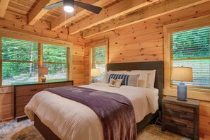 A wooden cabin bedroom with a bed, bedside tables, and windows. - Beehive Bungalow *Charming Forest Escape* Hot Tub (Logan)
