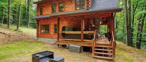A wooden cabin with a deck, a grill, and a stone pathway.