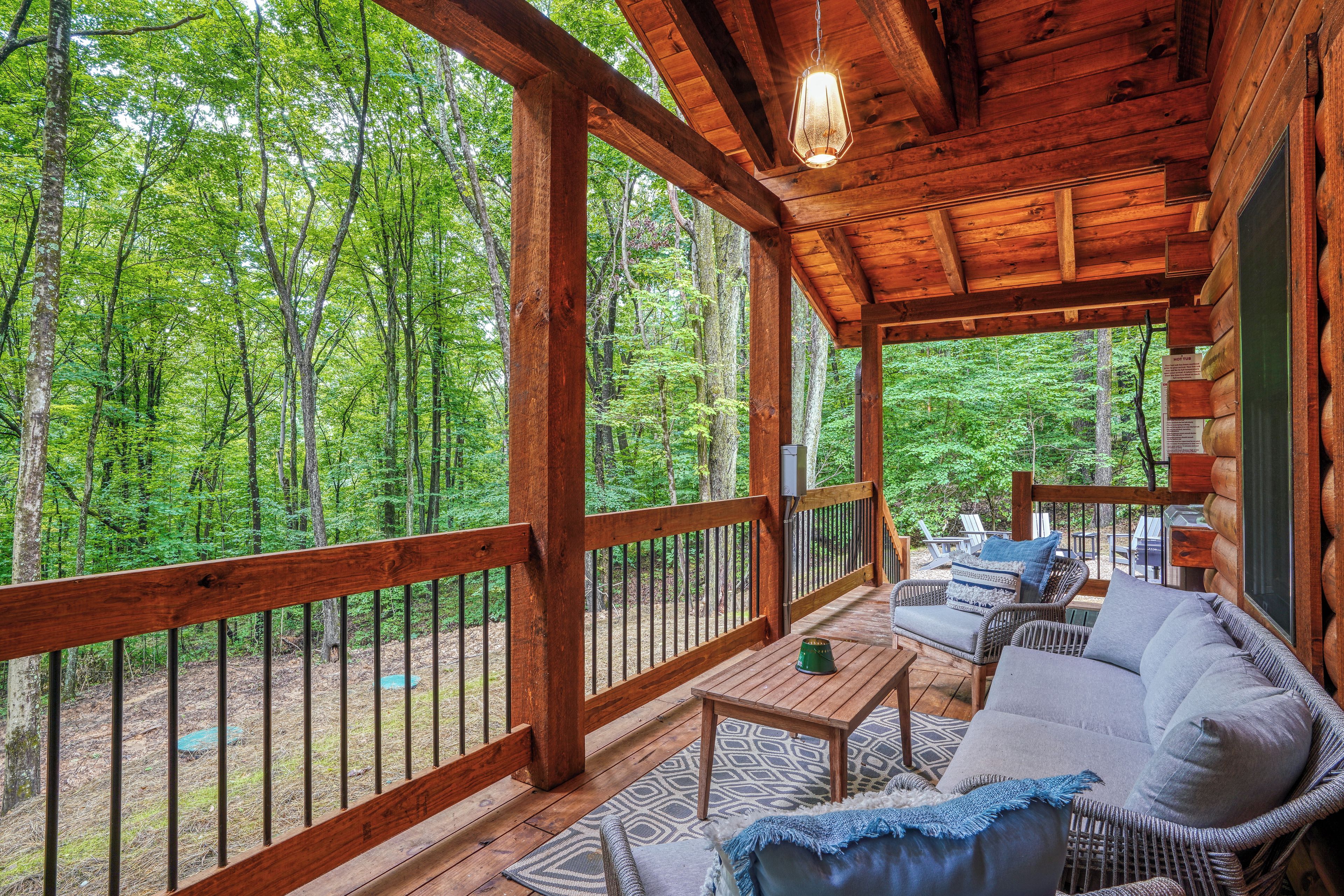 A wooden deck with a sofa and a table, surrounded by a wooden railing, overlooking a forest.