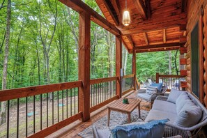 Une terrasse en bois avec un canapé et une table, entourée d’une balustrade en bois, donnant sur une forêt.
