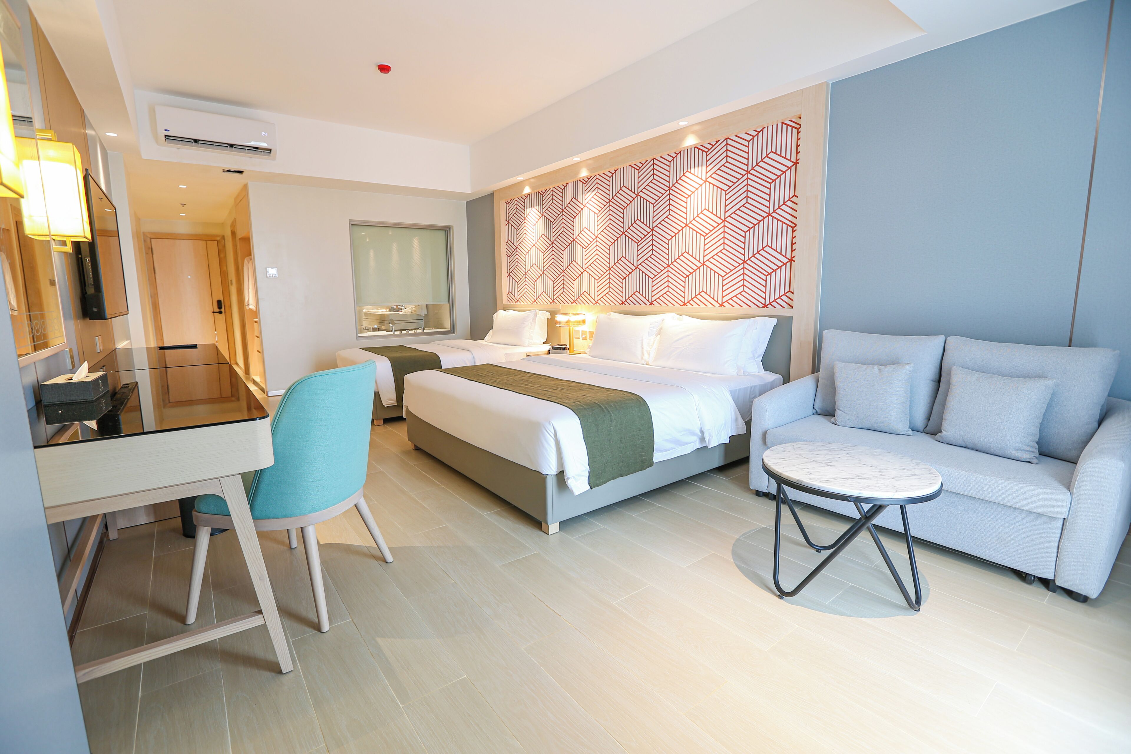 A modern hotel room with a bed, a sofa, a small table, a desk, and a chair.