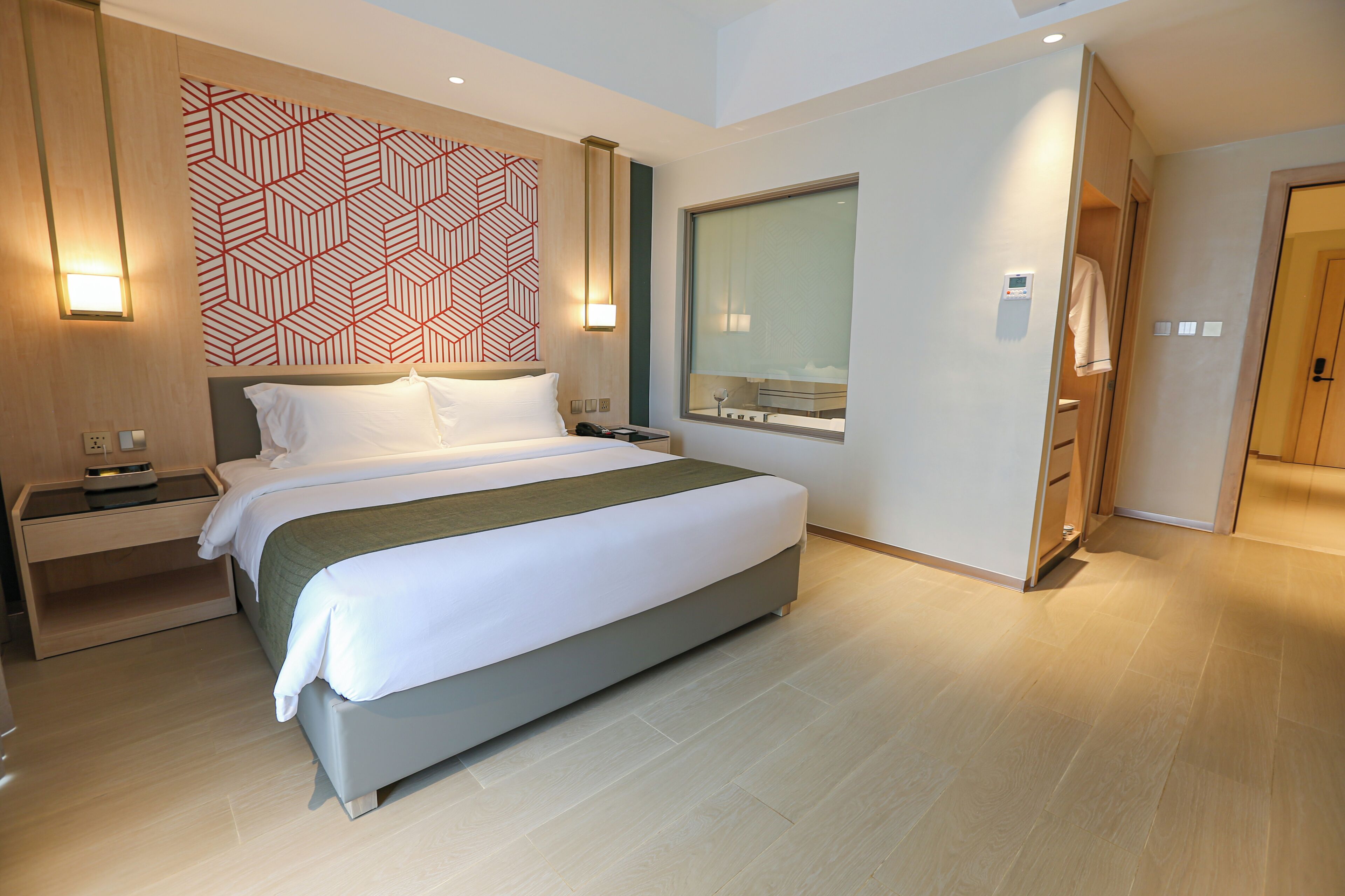 Una habitación de hotel moderna con una cama grande, mesitas de noche, un televisor de pared y un ventanal amplio.