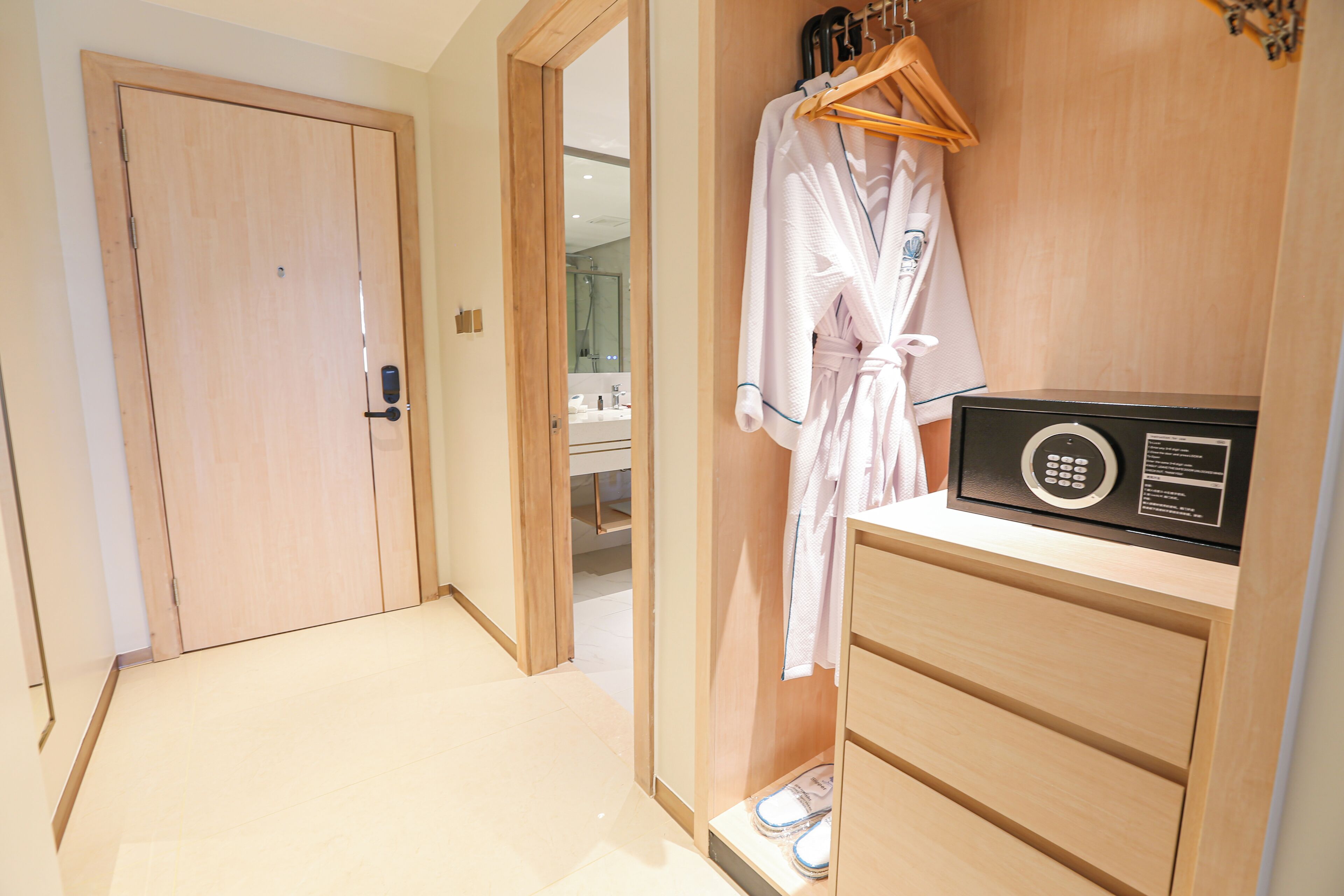 Habitación de hotel con un armario de madera, una bata colgada en la pared y un zapatero.