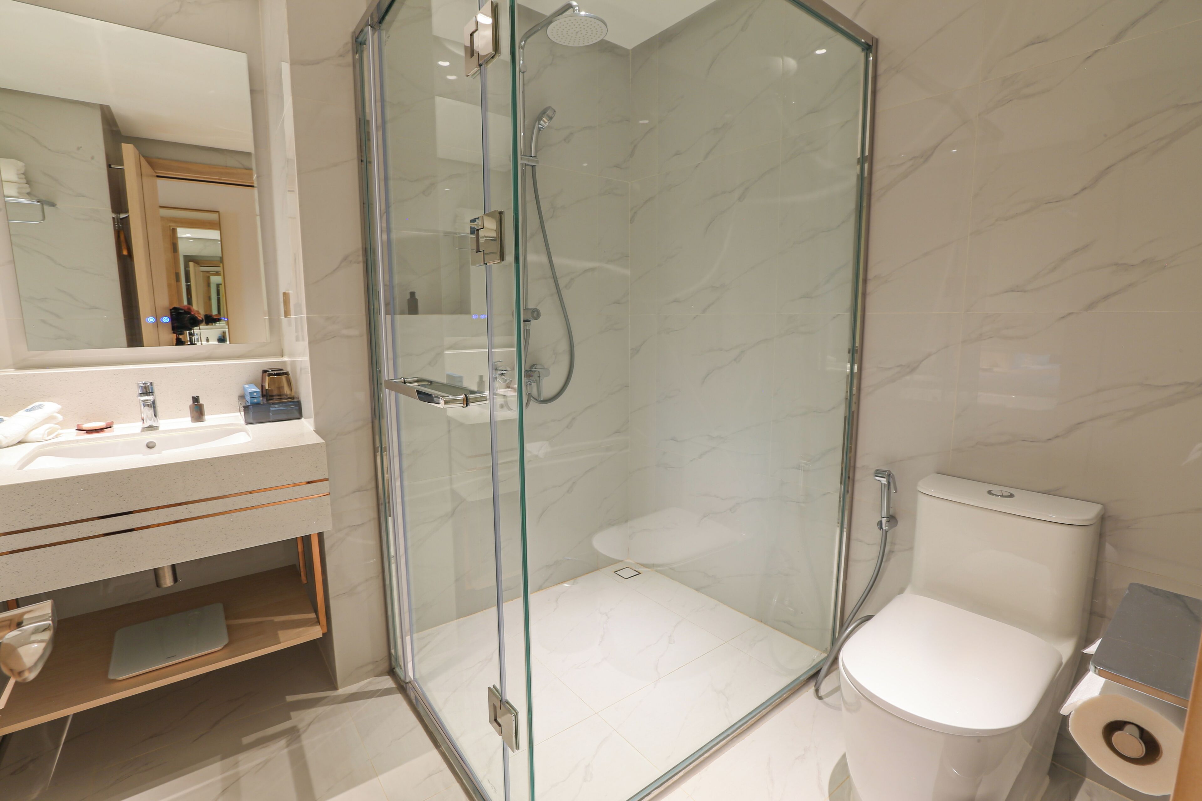 A modern bathroom with a glass-enclosed shower, a toilet, and a sink with a mirror above.