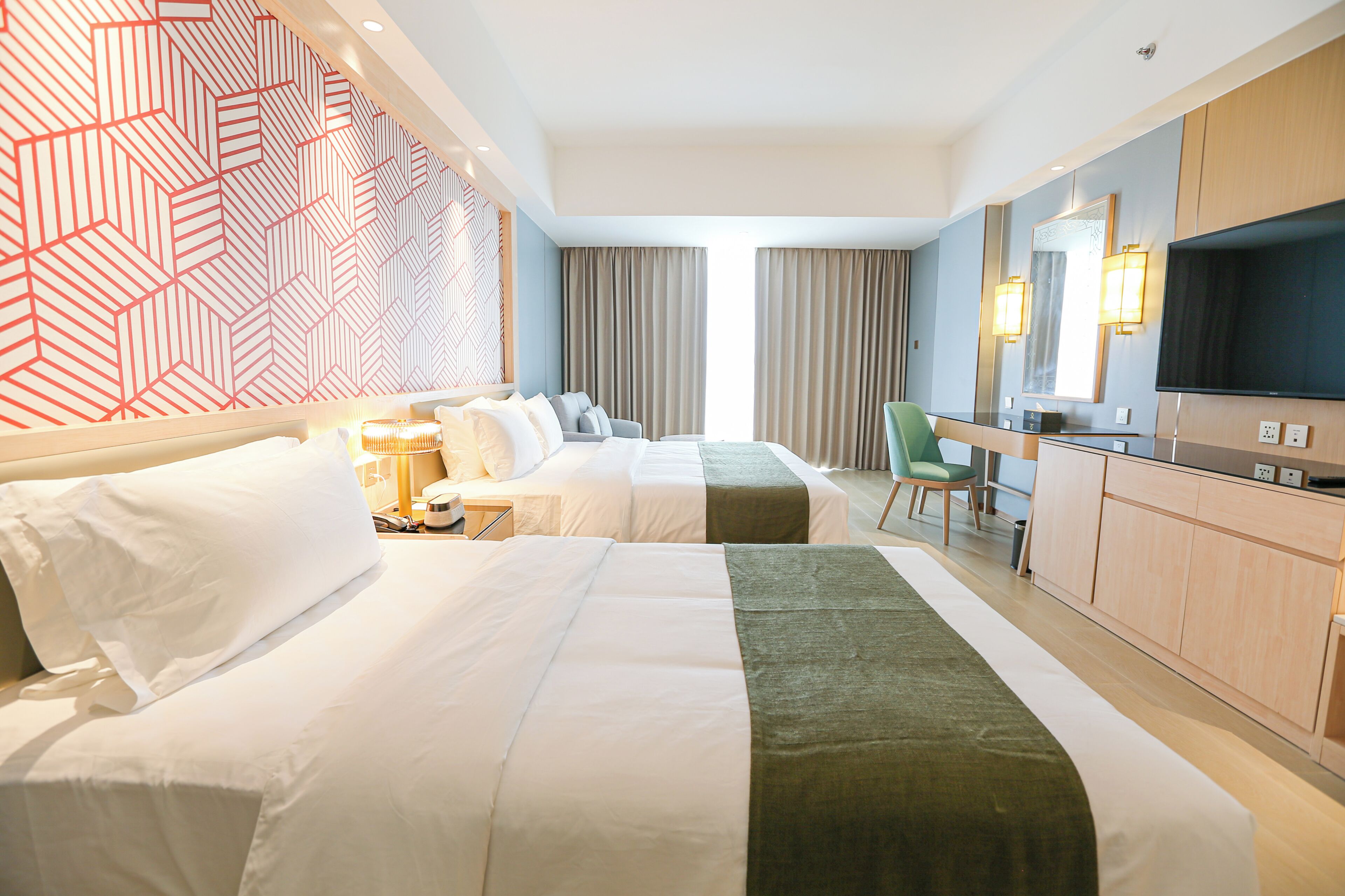 A hotel room with two beds, a desk, a chair, a TV, and a minibar.