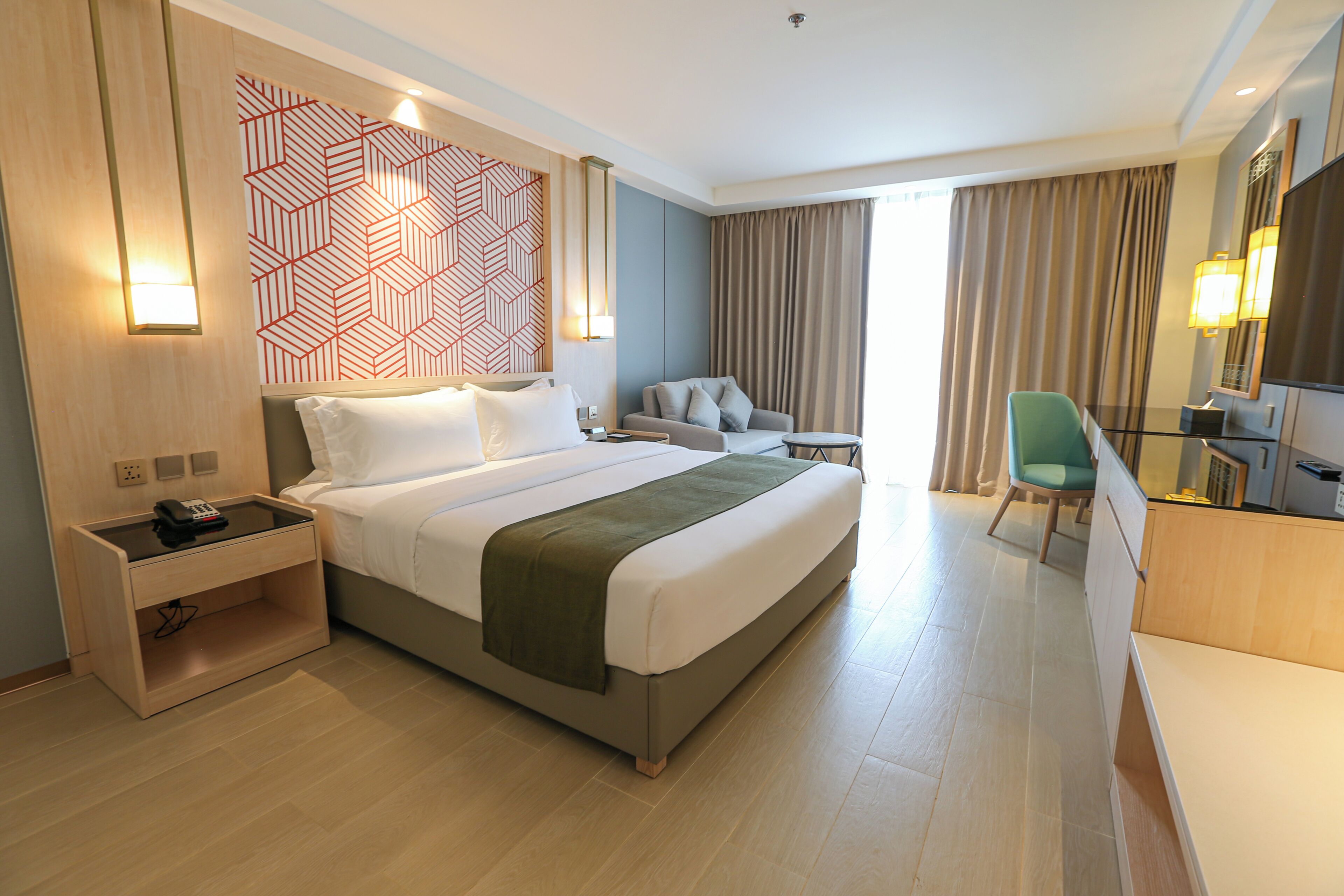 A hotel room with a bed, bedside table, lamp, chair, and a large mirror.