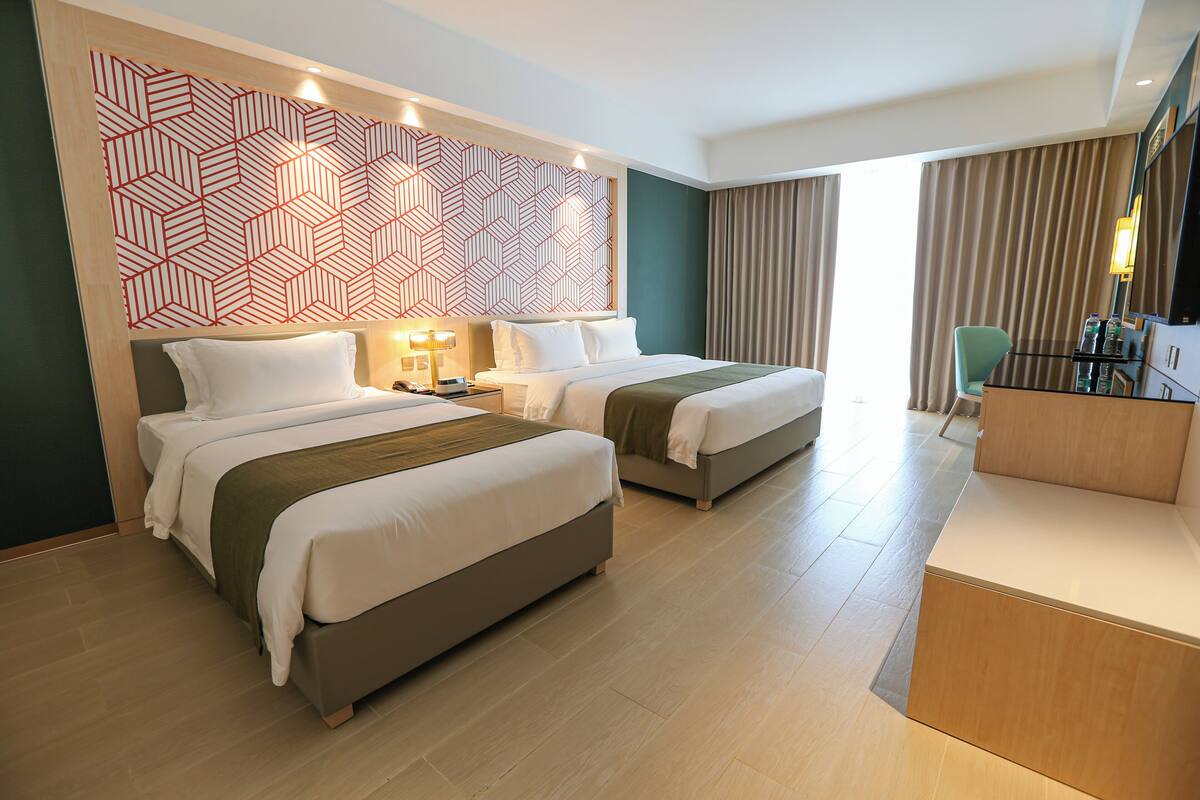 Ein Hotelzimmer mit zwei Betten, einem Schreibtisch, einem Stuhl und einer Wand mit großem geometrischem Muster.