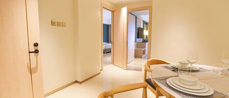 A hotel room with a dining table set for two, a wooden door, and a hallway leading to another room.