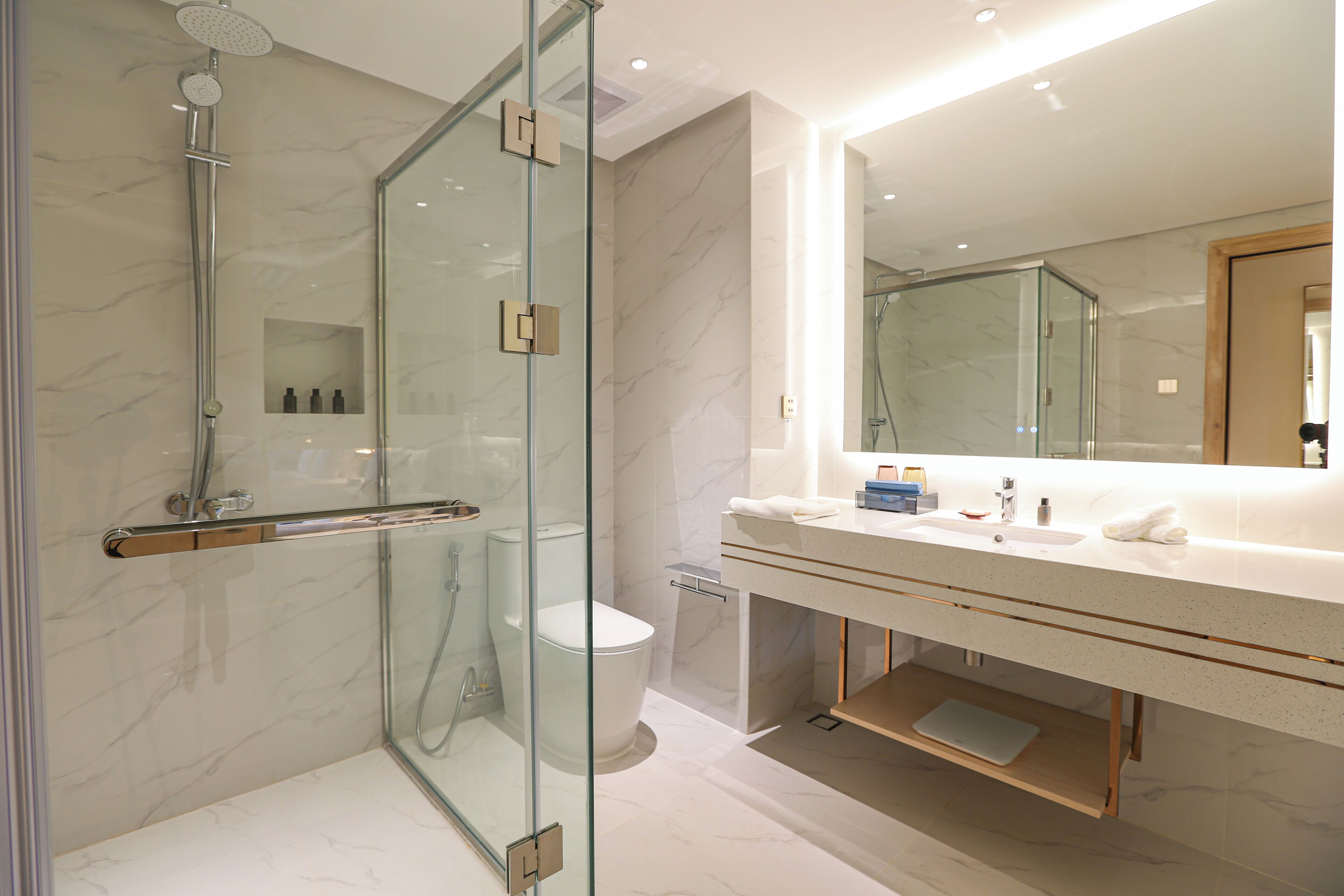 A modern bathroom with a glass-enclosed shower, a white marble vanity, and a large mirror.