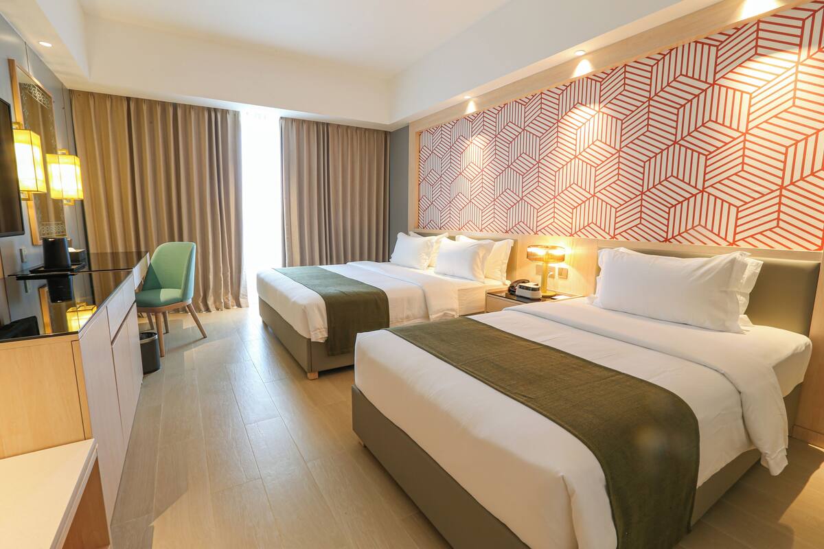Ein Hotelzimmer mit zwei Betten, einem Schreibtisch, einem Stuhl und einer Wand mit geometrischem Muster.