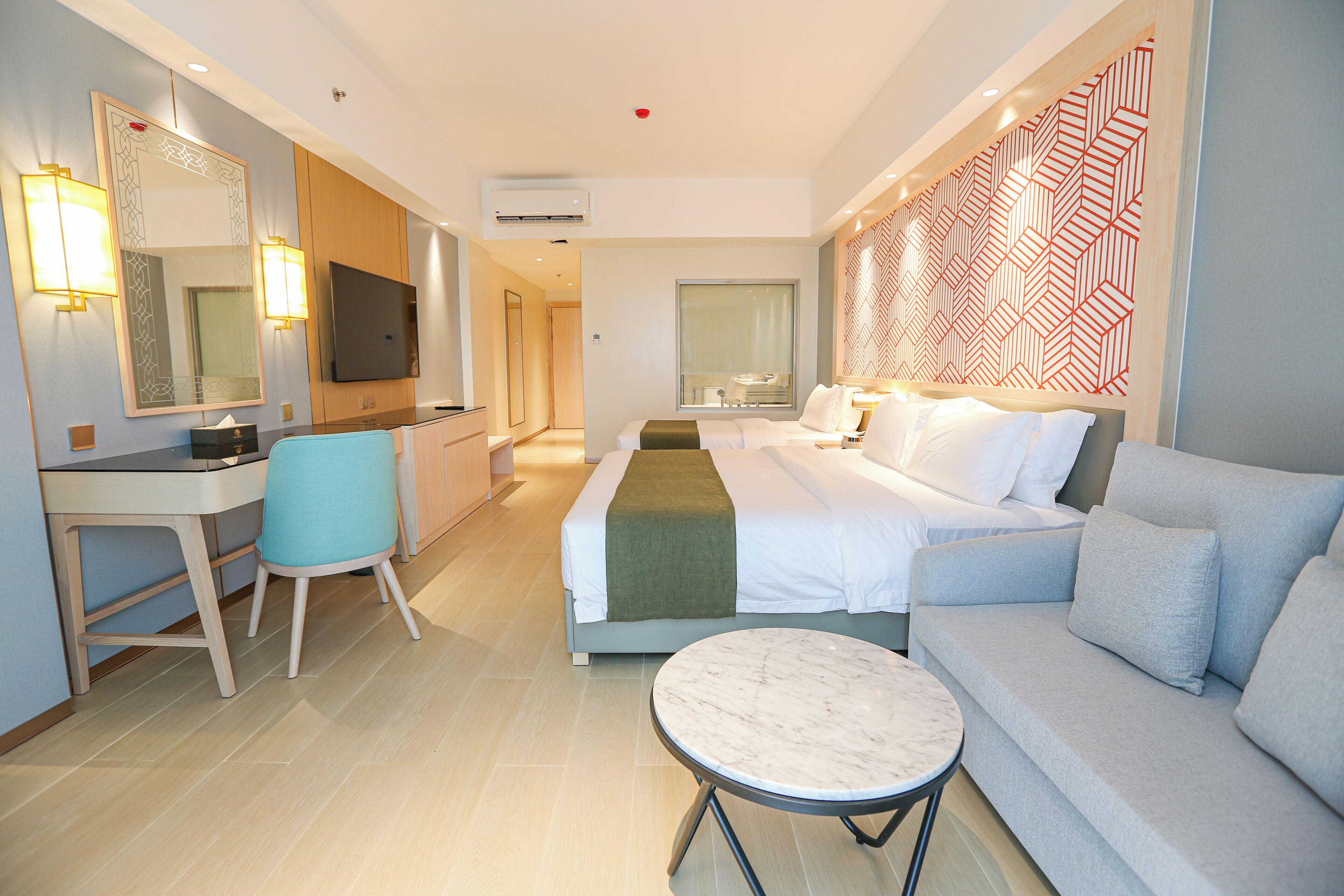 Hotelkamer met een bed, een slaapbank, een bureau, een stoel, een televisie en een behang met patroon.