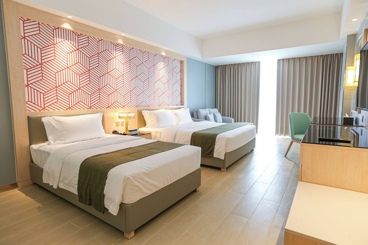 Ein Hotelzimmer mit zwei Betten, einem Schreibtisch, einem Stuhl und einer Wand mit Muster.