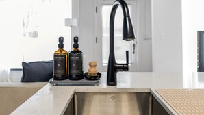 A kitchen with a modern faucet, two bottles of dish soap, and a wooden brush on the countertop. - Modern Loft in Vibrant Downtown Royal Oak - Just a Block Away! (Royal Oak)