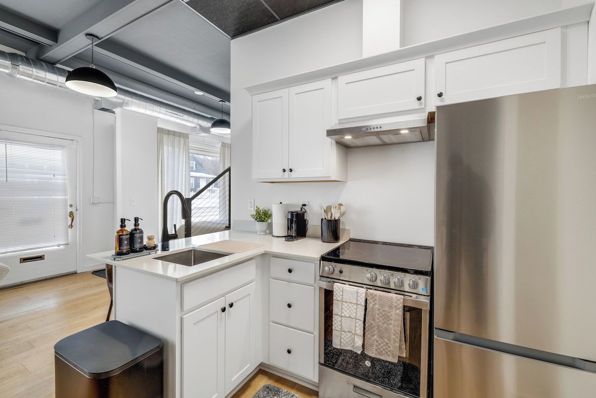 A modern kitchen with white cabinets, a stainless steel refrigerator, a black stove, and a sink.