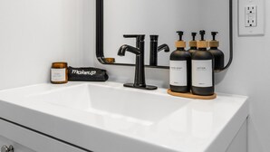 A bathroom with a white sink, black faucets, and two bottles of lotion and hand soap. - Modern Loft in Vibrant Downtown Royal Oak - Just a Block Away! (Royal Oak)