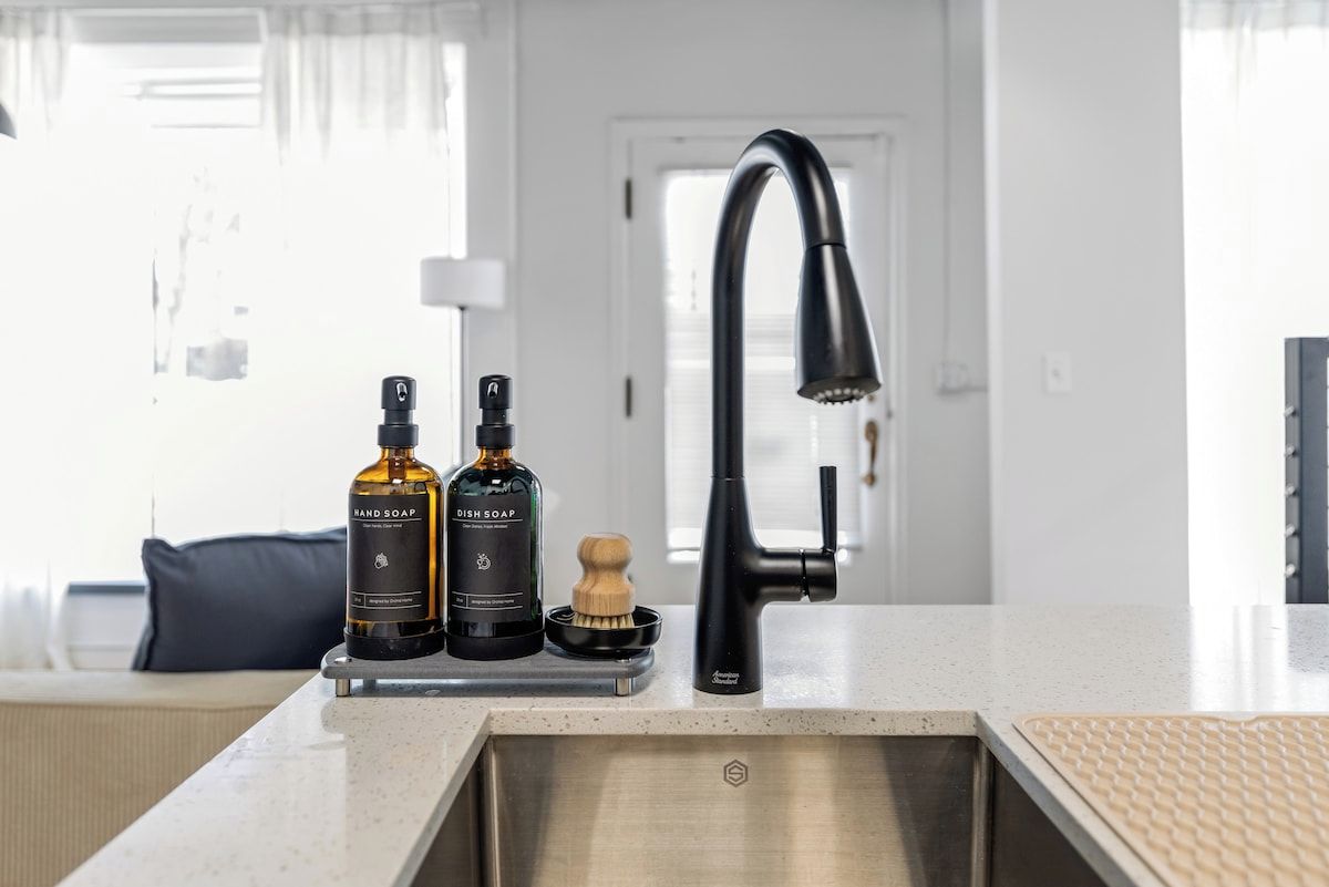 A kitchen with a modern faucet, two bottles of soap, and a wooden brush on the counter.