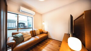 Un salon moderne avec un canapé en cuir, un lampadaire et un téléviseur à écran plat posé sur un meuble en bois.