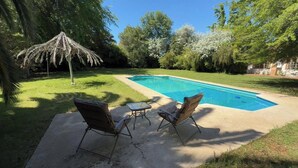 A backyard with a swimming pool, two lawn chairs, a small table, and a tiki umbrella.