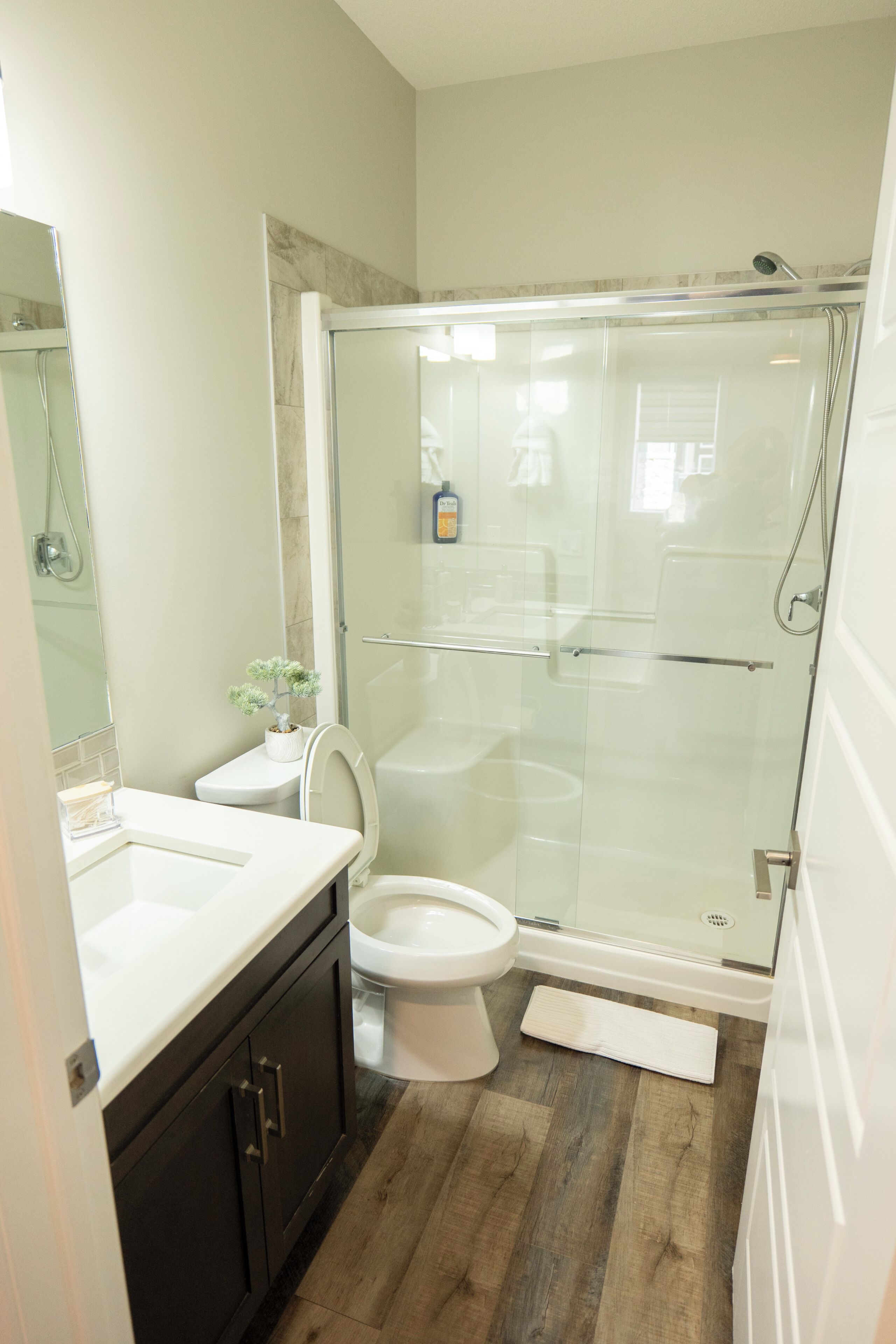 A bathroom with a glass-enclosed shower, a toilet, and a sink with dark cabinets.