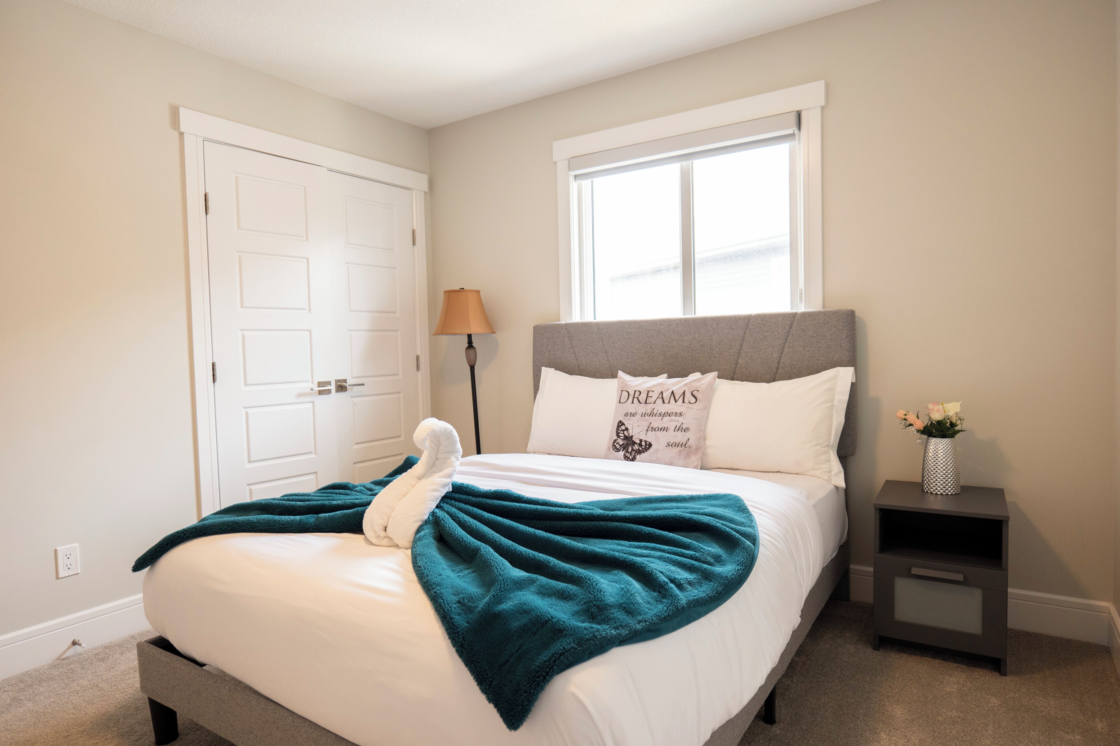 A bedroom with a bed, a nightstand, a window, and a door.