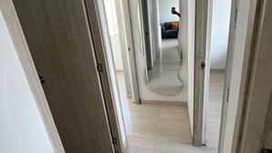 Ein Flur mit Holztüren, gefliestem Boden und einem Spiegel, der ein Zimmer mit einem blauen Sofa zeigt.