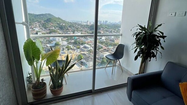Ein modernes Wohnzimmer mit einem großen Schiebeglasfenster, das auf einen Balkon führt, einem blauen Sofa und Topfpflanzen.