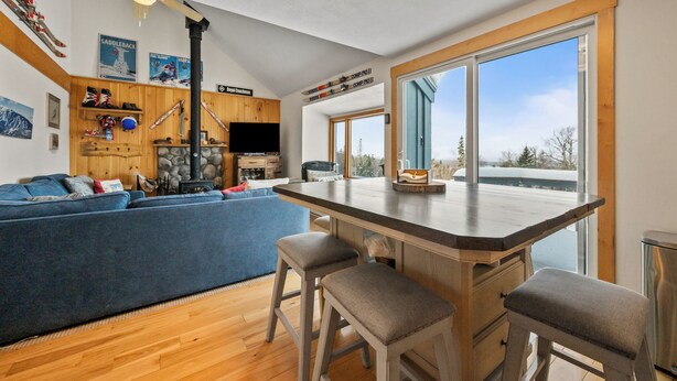 A modern kitchen with wooden accents, a large window, and a stone fireplace. - White Birch 58 - Ski in/out Condo, Pet friendly! (Rangeley)