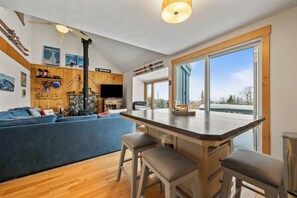 A modern kitchen with wooden accents, a large window, and a stone fireplace. - White Birch 58 - Ski in/out Condo, Pet friendly! (Rangeley)