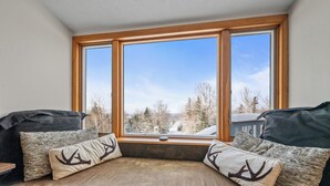 A cozy seating area with a view of a snowy landscape through large windows. - White Birch 58 - Ski in/out Condo, Pet friendly! (Rangeley)